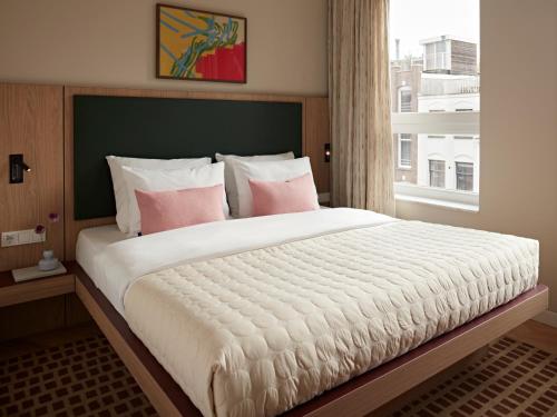 a bedroom with a large bed with pink pillows and a window at Numa Amsterdam Vondelpark in Amsterdam