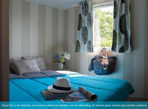 Un dormitorio con una cama azul con un sombrero y una ventana. en Siblu Camping in de Bongerd, en Oostkapelle