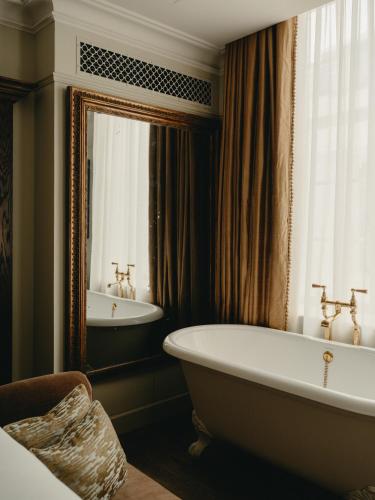 a bathroom with a tub and a sink and a mirror at The Ned in London
