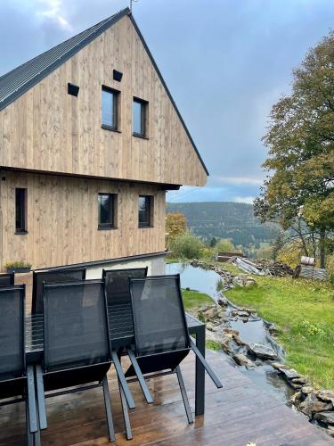 a house with two chairs on a deck next to a river at Apartmány nora - Příchovice in Kořenov