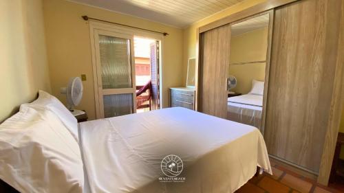 Un dormitorio con una cama blanca y un espejo. en Sobrado aconchegante próximo do mar, en Passo de Torres