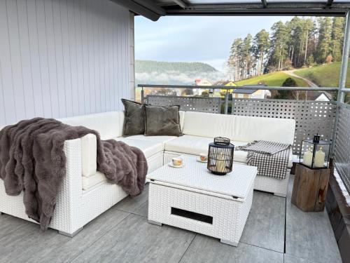 Serenity Stay Baiersbronn Kamin und Schwarzwaldblick في بايرسبرون: أريكة بيضاء وطاولة على شرفة