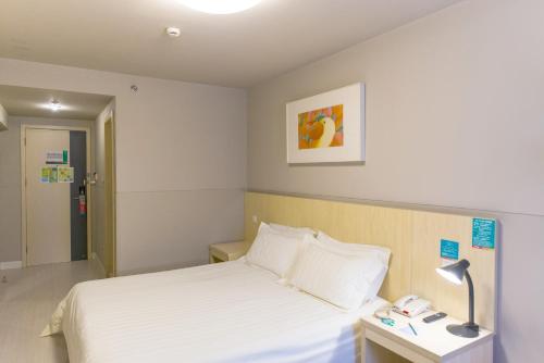 a bedroom with a bed and a lamp on a table at Jinjiang Inn Qingdao Cangkou Park in Qingdao