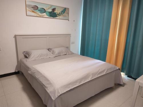 ein weißes Bett in einem Zimmer mit blauen Vorhängen in der Unterkunft Jianjia Homestay in Zhengzhou