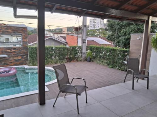 a patio with two chairs and a swimming pool at Casa com piscina, suite com hidro em Blumenau in Blumenau