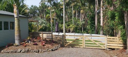 Una valla de madera delante de una casa con palmeras. en Darwin Cottage, en Kerikeri