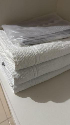 a stack of white towels sitting on top of a bed at Quarto com ar banheiro frigobar in Sinop