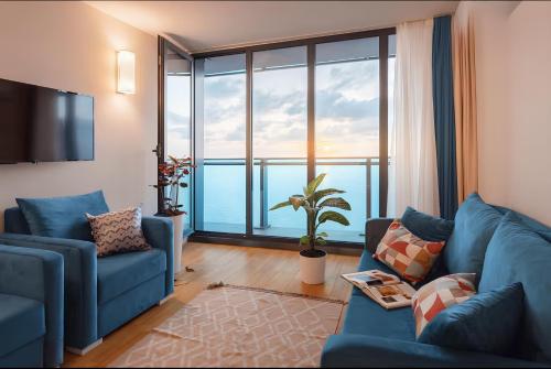 Una sala de estar con un sofá azul y una ventana grande. en Panorama Luxurious with sea view Hotel, en Batumi
