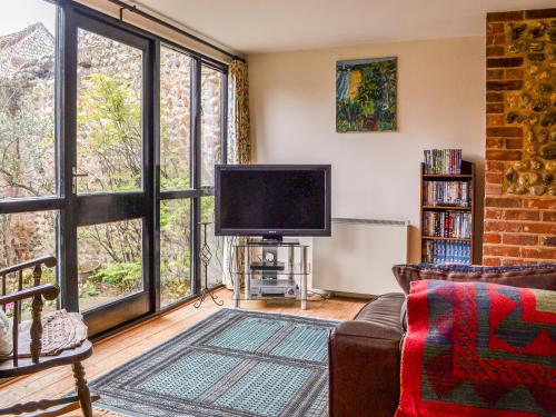 a living room with a tv and large windows at Owl Barn in Sidestrand