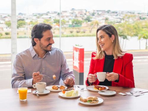 瓜拉普阿瓦ibis Guarapuava的坐在餐桌上吃早饭的男人和女人