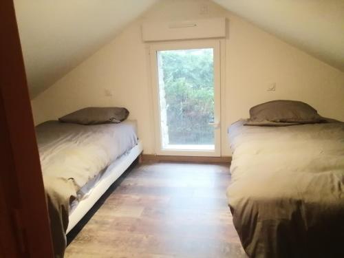 two beds in a room with a window at Maisonnette meublée à la campagne in Ernée