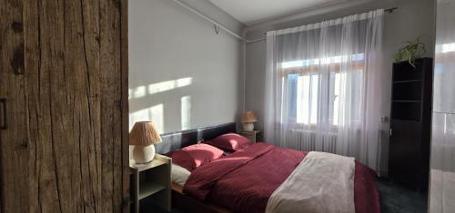 a bedroom with a bed with red sheets and a window at White House Apartment in Jūrmala
