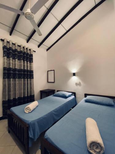 two beds in a bedroom with blue sheets at Chandra Holiday Home Hiriketiya in Dickwella