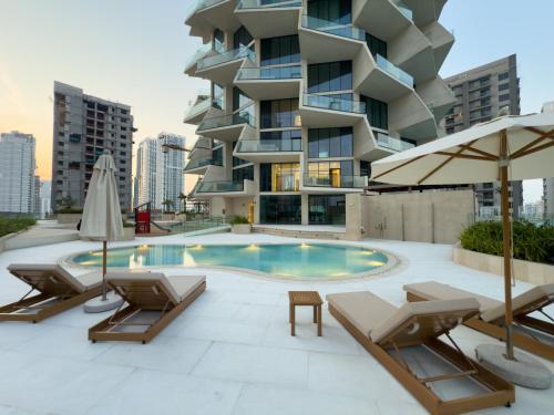 a building with a swimming pool with chairs and umbrellas at Private Pool - Amazing 1BR Apartment in JVC in Dubai