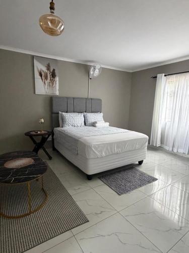 Un dormitorio con una cama blanca grande y una mesa en Ella Guest House, en Pretoria