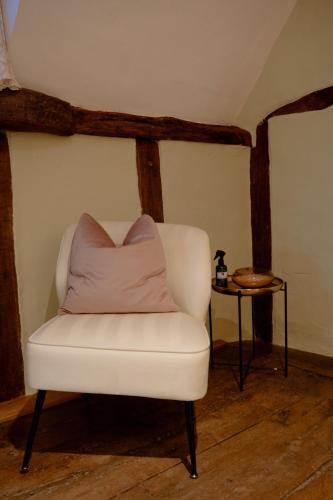 a white chair with a pink pillow next to a table at The Cotswold Luxe Cottage in Framlingham