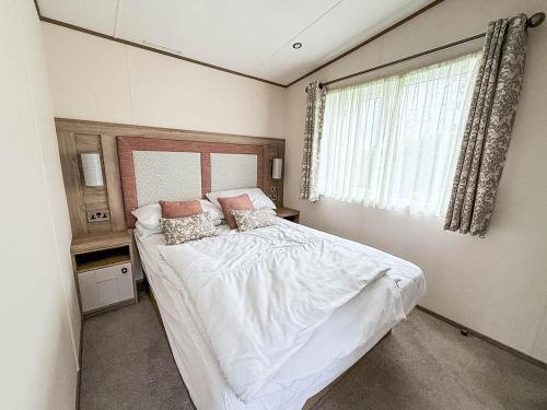 Stunning 8 Berth Caravan With Decking At Kessingland Beach Ref 90017D في Benacre: غرفة نوم بها سرير بملاءات بيضاء ونافذة
