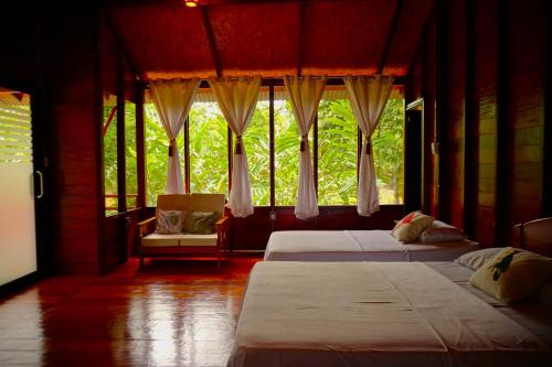 Passiflora Lodge Tambopata في بويرتو مالدونادو: سريرين في غرفة بها نوافذ وكرسي