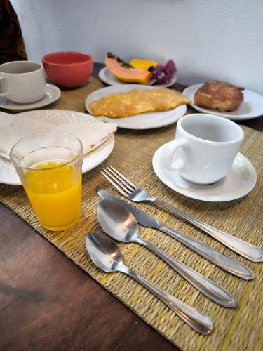 a table with plates and utensils and a cup of orange juice at Pousada Vilarejo in Caraíva