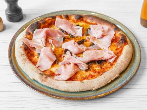 Una pizza con jamón encima en un plato. en Novotel Rouen Centre Cathédrale, en Rouen