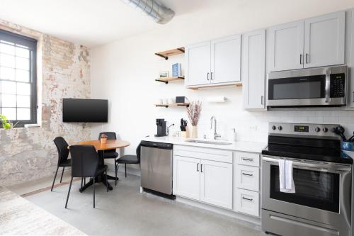 Brewery District 2-Story 2BR Apt Near Fiserv with Rooftop, Gym, and Parking في ميلووكي: مطبخ مع دواليب بيضاء وطاولة مع كراسي