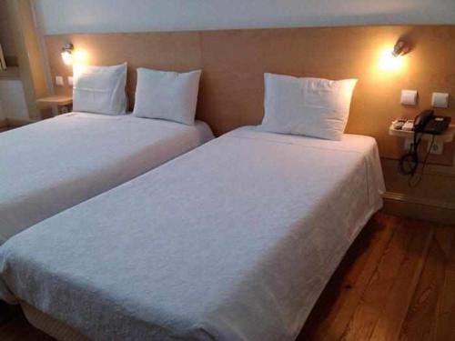 two white beds in a hotel room with a phone at Internacional in Coimbra