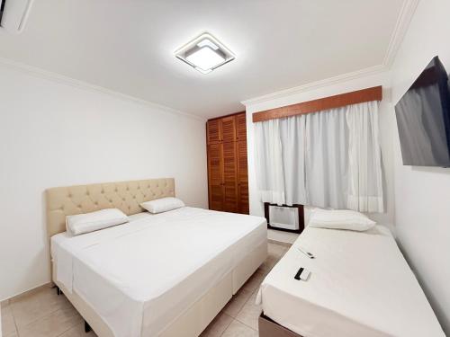 a bedroom with two beds and a tv at Flat estudio 110 Amarilis Riviera de São Lourenço, 03 piscina climatizada, serviço de hotelaria, limpesa e troca de toalhas diária, carregador veiculo elétrico e servico de praia finais de semana WiFi 500 in Riviera de São Lourenço