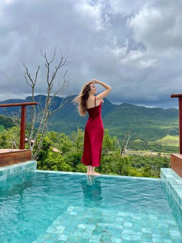a woman in a red dress standing on the edge of a swimming pool at Vila Rosa Lodges - Chalés e Domo in Praia Grande