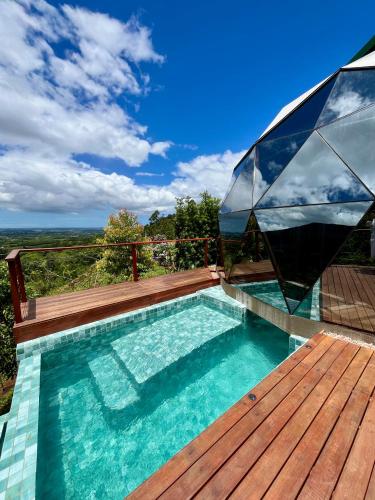 a swimming pool with a wooden deck and a glass house at Vila Rosa Lodges - Chalés e Domo in Praia Grande