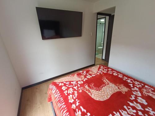 a bedroom with a bed with a red blanket and a tv at Alojamiento Cómodo y Hermoso en apartamento 7 personas Carnavales in Pasto
