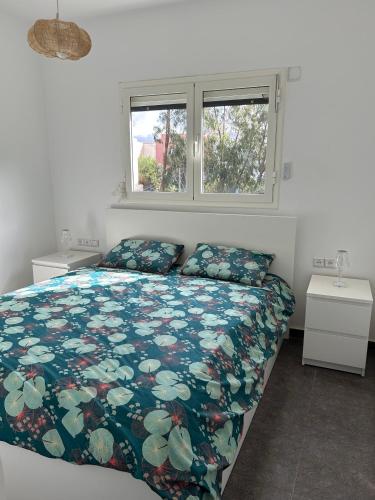a bedroom with a bed with a floral comforter and two windows at appartement Topaze in Essaouira
