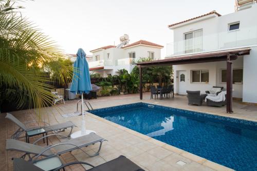 a swimming pool with chairs and an umbrella next to a house at Carolyn Villa is a Luxury 4-Bedroom Villa with Private Pool in Ayia Napa in Ayia Napa