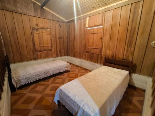 two beds in a room with wooden walls at Sitio alto valinhos in Itamonte