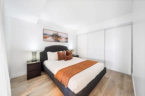 a bedroom with a large bed with white walls and wooden floors at Spacious Downtown Condo - Walk to CN Tower & More in Toronto