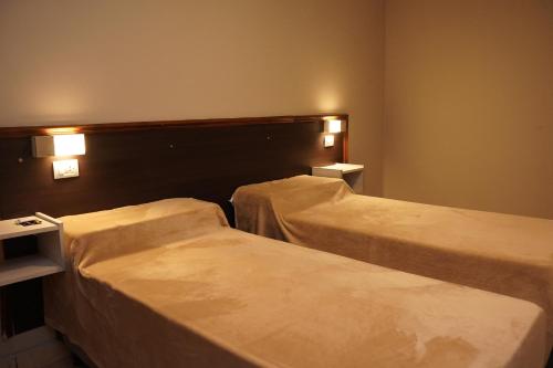 twee bedden in een hotelkamer met verlichting aan de muur bij Hotel Haití in San Miguel de Tucumán