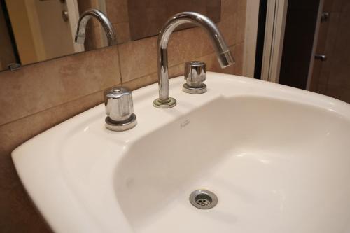 een witte wasbak met twee kranen en een spiegel bij Hotel Haití in San Miguel de Tucumán