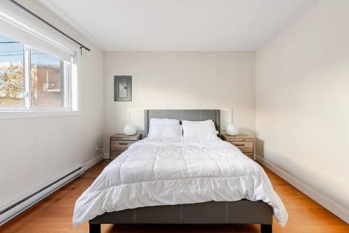 a white bedroom with a large bed and a window at Voltaire 2 Appartement 4,5 , 2ch Laval, Canada meublé in Laval