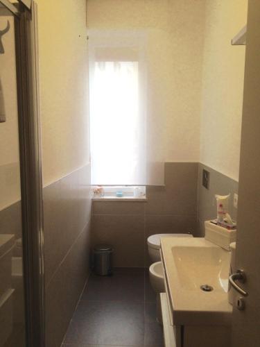 a bathroom with a toilet and a sink and a window at Lilly Rose Apartment in Alba