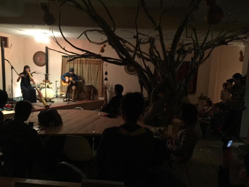 a group of people sitting around a stage with a tree at Guest House & Cafe Ohana in Imabari