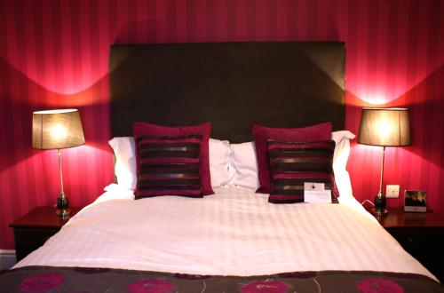 a bedroom with a large bed with red walls and two lamps at Belmont Hotel Leicester in Leicester