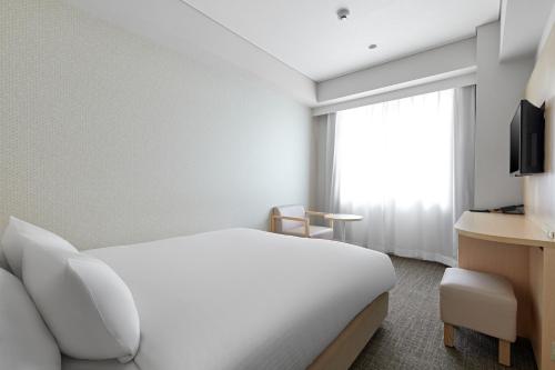 a hotel room with a white bed and a window at Sotetsu Fresa Inn Kyoto-Hachijoguchi in Kyoto