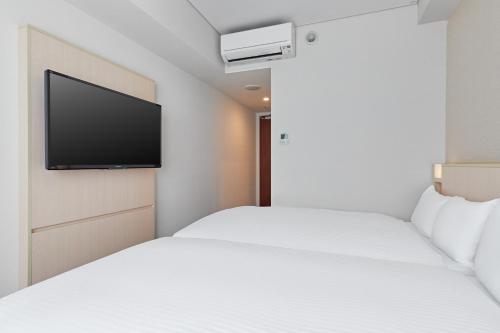 a hotel room with two beds and a flat screen tv at Sotetsu Fresa Inn Kyoto-Hachijoguchi in Kyoto