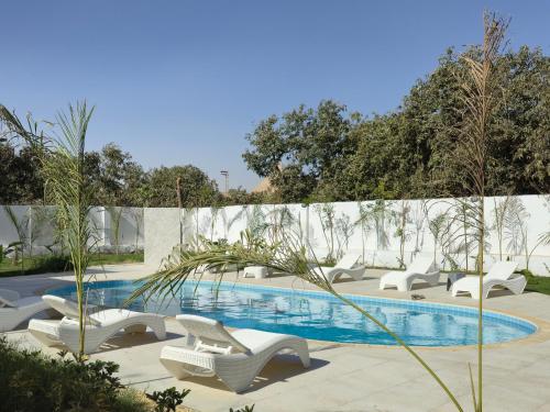 a swimming pool with white chairs and a fence at Nakhil Pyramids Resort in Cairo