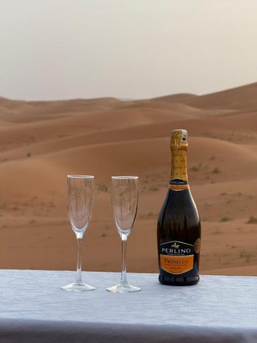 a bottle of champagne and two glasses on a table in the desert at Camel luxury camps Merzouga in Merdani