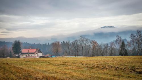 a house in the middle of a field with trees and clouds at Chata Kačerov in Kašperské Hory