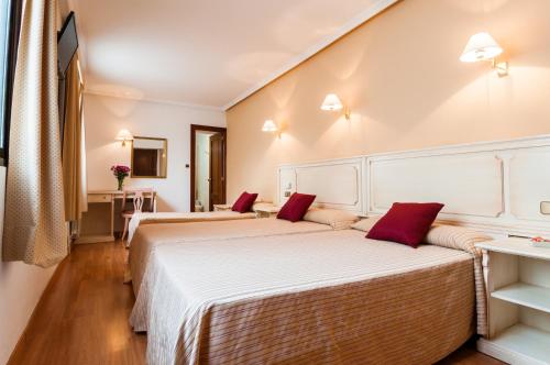 two beds in a hotel room with red pillows at Hotel Victoria in Linares