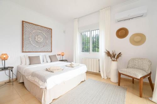 een witte slaapkamer met een bed en een stoel bij Casa de las Montañas in Parcent