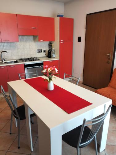 Roero House في Canove: مطبخ بخزائن حمراء وطاولة بيضاء مع مزهرية من الزهور