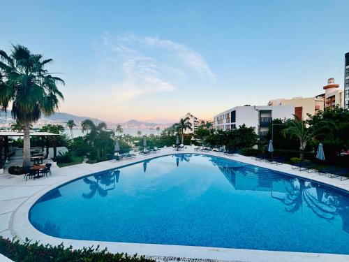 a large blue swimming pool with palm trees and buildings at SUITE INTI vista al mar in Acapulco