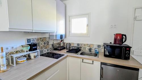 a kitchen with white cabinets and a sink and a microwave at Le Plein Sud - Carqueiranne in Carqueiranne